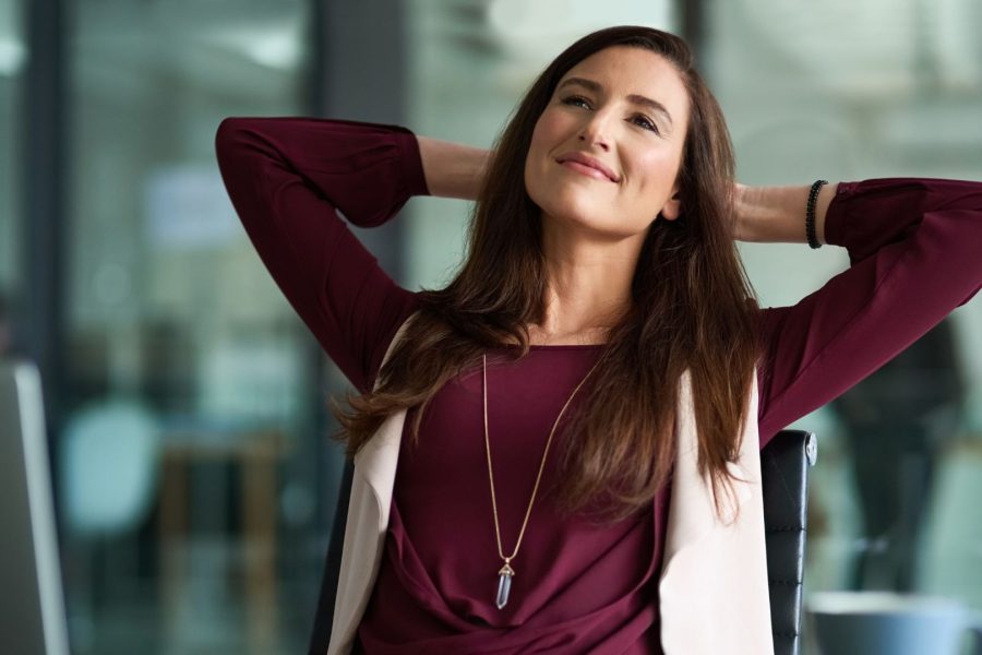 A young woman leaning back in the chair looking pleased that she has secured comfortable retirement with Thinking Wealth.