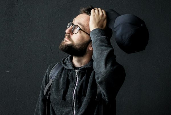 Picture of a man in black background holding a cap and thinking_ feature image for Thinking-Wealth-Blog_Investing: Give, Take, Make, and the In-Betweens